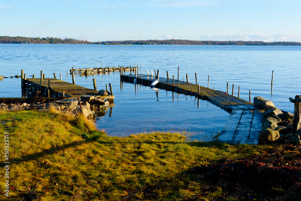 Calm and motionless water surround some piers in the archipelago. The morning winter sun is slowly thawing the grass. Location Kuggeboda near Ronneby in Sweden.