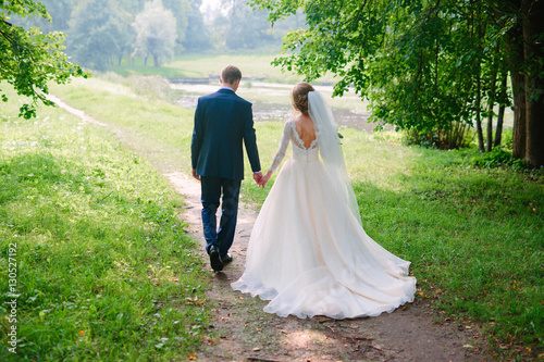 Slika na platnu Just married loving hipster couple in wedding dress and suit on a green field in the woods