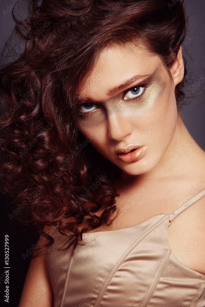 Portrait of young beautiful girl with curly messy hair and fanct golden make-up