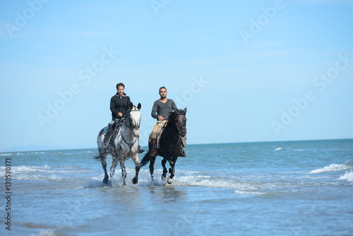 happy young couple vacation riding horses on the beach in a sunny summer day