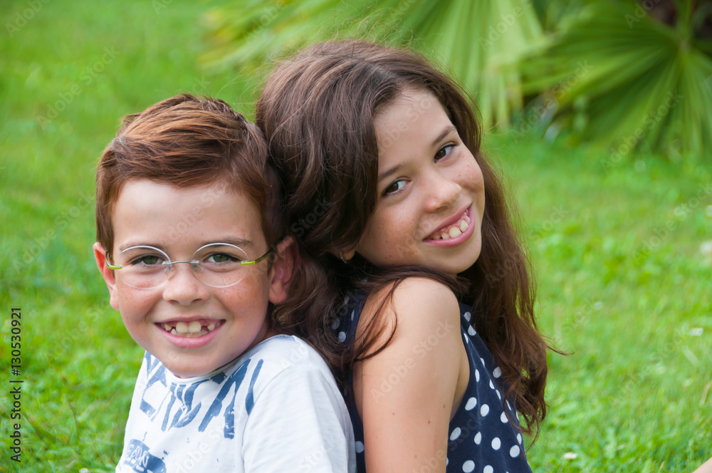 Two children sitting outdoors on grass in summer Two children sitting outdoors on grass in summer