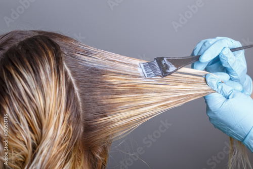 Professional hairdresser dyeing hair of her client in salon. Selective focus.