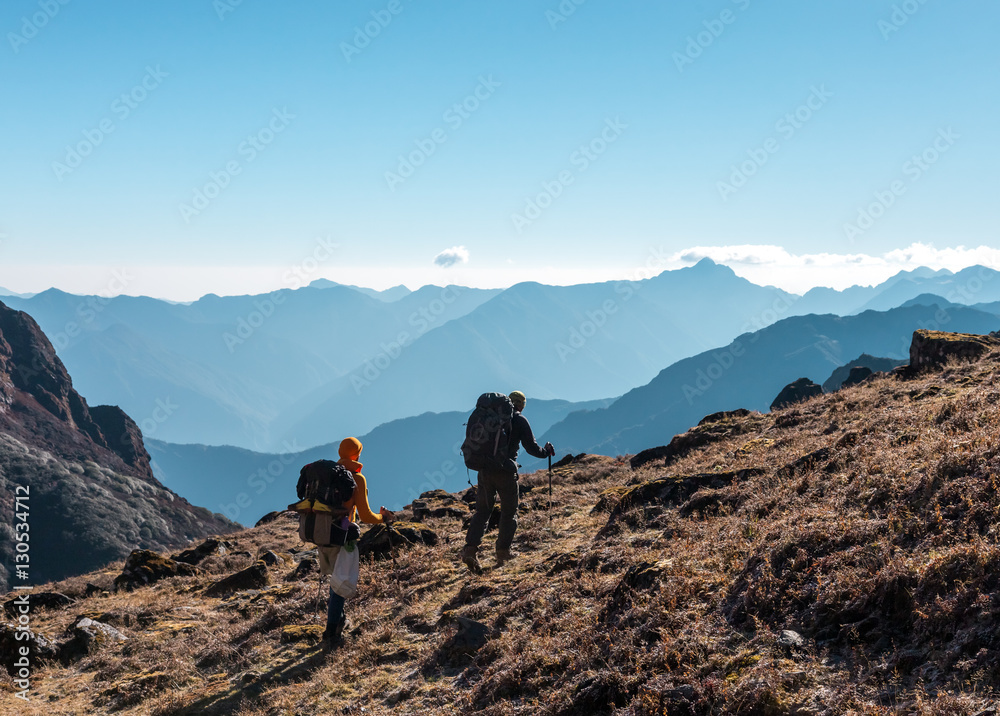 Two Hikers with Backpacks walking on grassy heel in Mountains