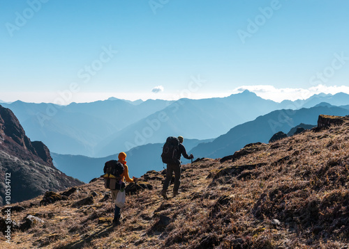 Two Hikers with Backpacks walking on grassy heel in Mountains