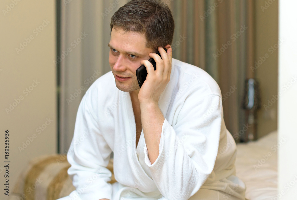 Man in bathrobe with mobile phone in hotel room.