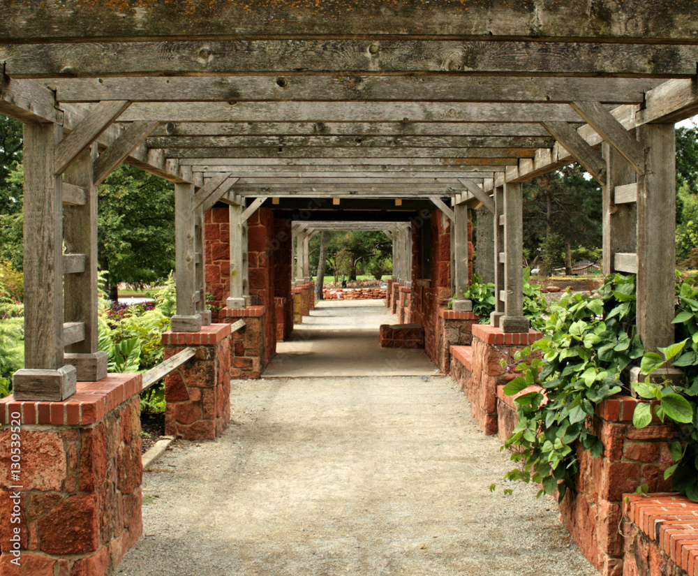 Fototapeta premium Weathered wood and brick rock arbor creates a tunnel in a green garden
