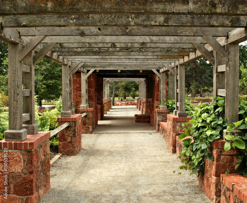 Fototapeta Naklejka Na Ścianę i Meble -  Weathered wood and brick rock arbor creates a tunnel in  a green garden