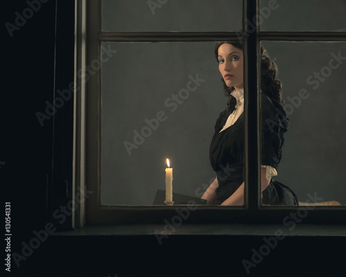 Foto Retro victorian girl reading book by candlelight behind window.