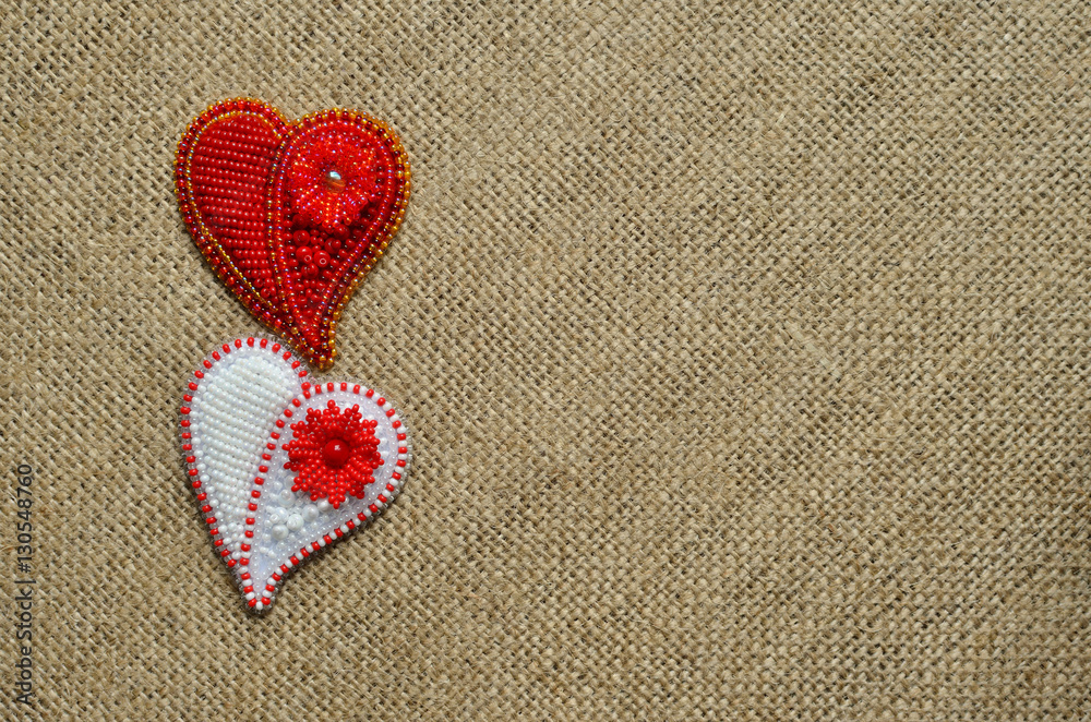 Two beaded jewellery hearts on a sackcloth. Top view. Left side. First red