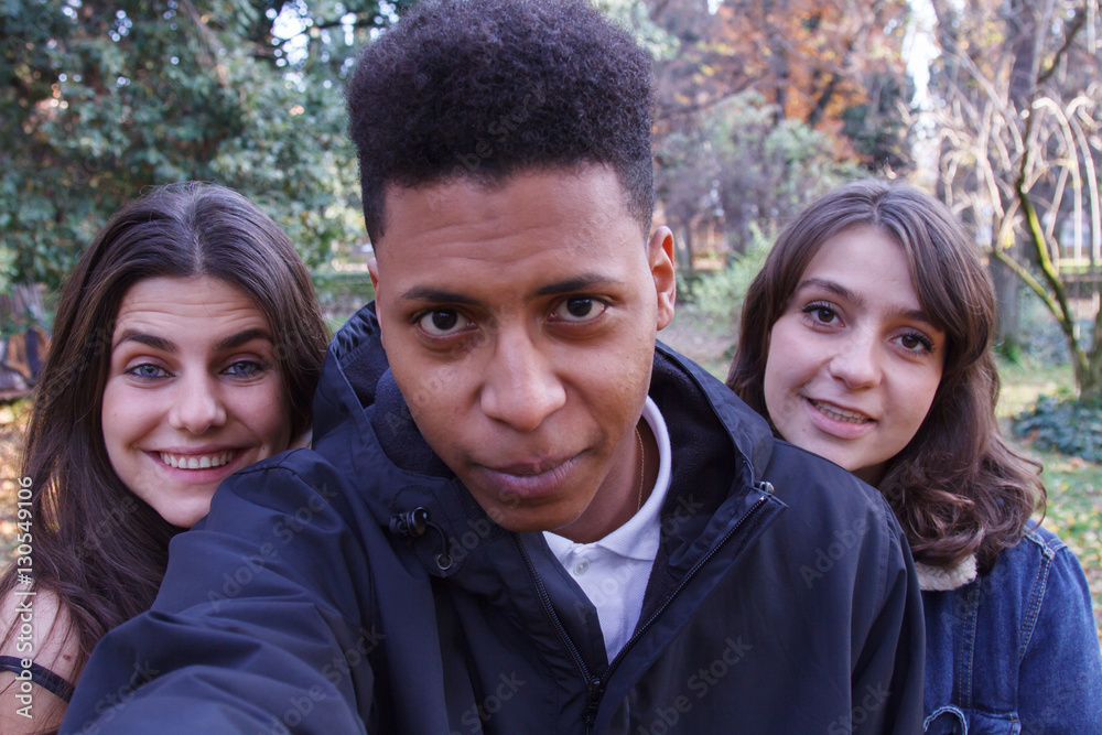 Young people of different races taking a selfie with the smartphone in the park. They are friends and enjoy a nice day outdoors. Young people of different races taking a selfie with the smartphone in the park. They are friends and enjoy a nice day outdoors.