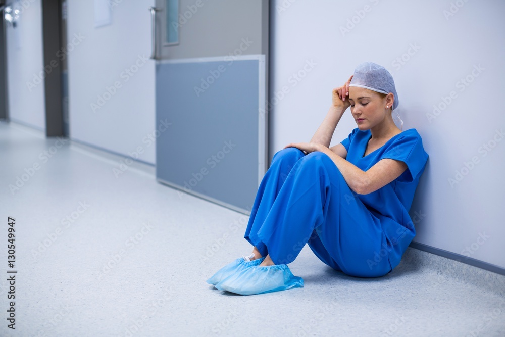 Tensed female nurse sitting in corridor Tensed female nurse sitting in corridor