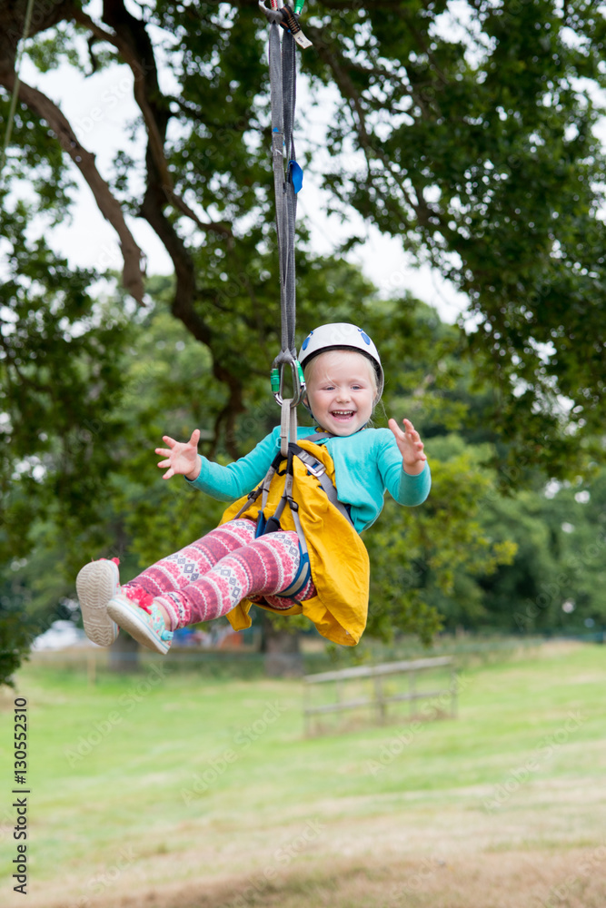 Laughing blonde child in helmet hangs from zip line Laughing blonde child in helmet hangs from zip line