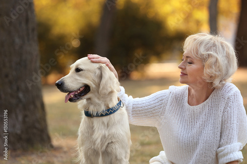 Senior woman and big dog sitting on grass in park
