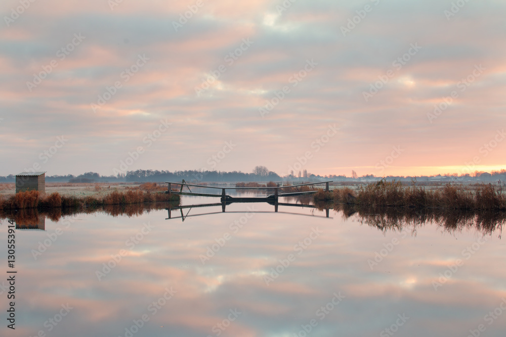 Weerspiegeling van zonsopkomst in poldersloot met bruggetje