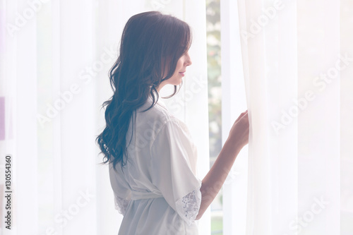 Beautiful woman in white silk robe standing near window Free Download Beautiful woman in white silk robe standing near window - GFXLoad