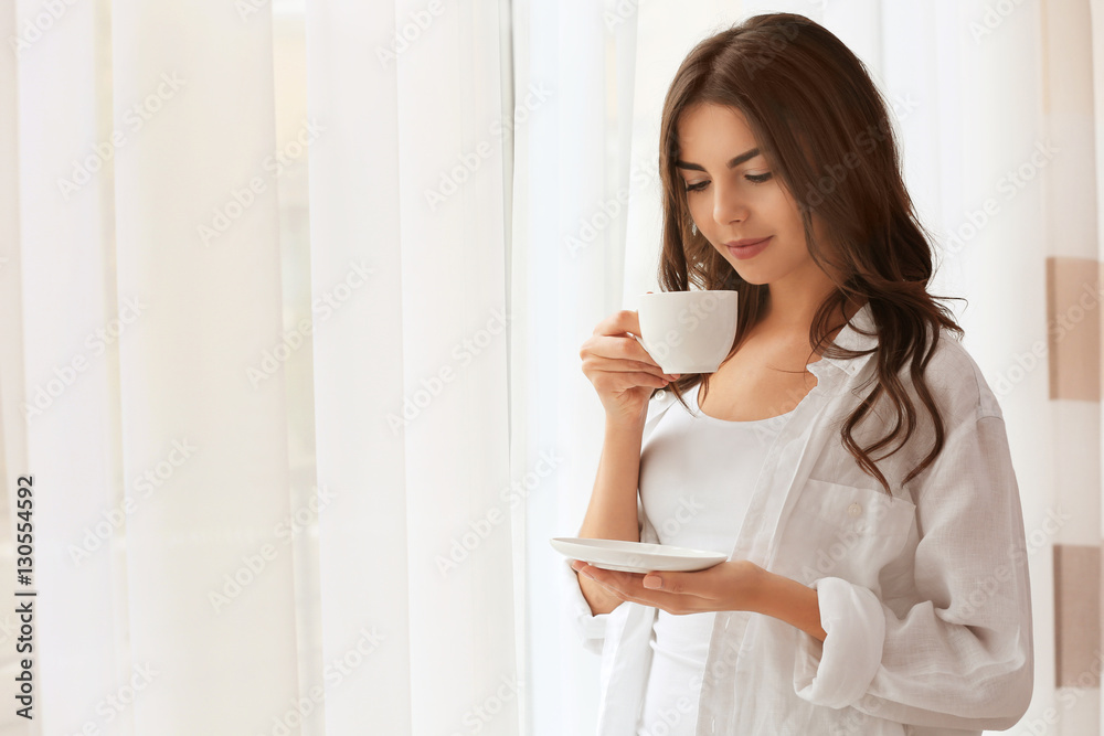 Beautiful woman with cup of aromatic coffee standing near window Beautiful woman with cup of aromatic coffee standing near window
