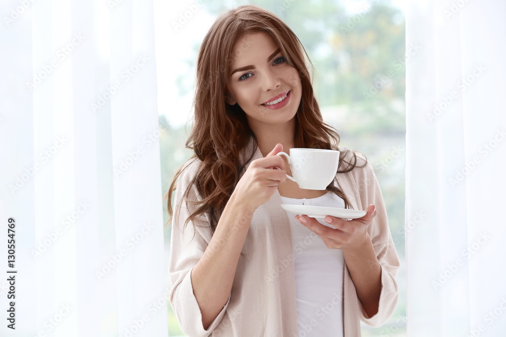 Beautiful woman with cup of aromatic coffee standing near window Beautiful woman with cup of aromatic coffee standing near window