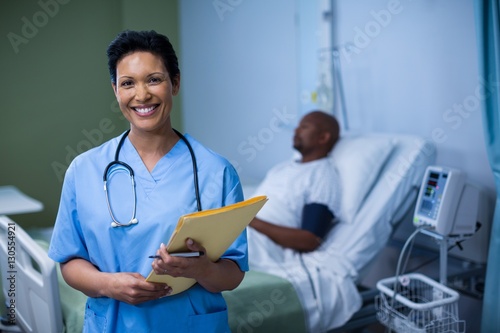 Portrait of female nurse standing with file in ward