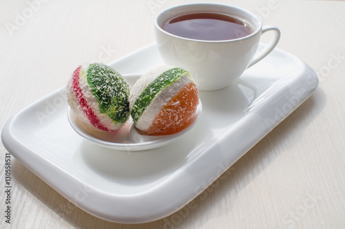 On the table a Cup of tea and candied fruit jelly in a white ceramic dish. Breakfast on a light background. High key. Selective focus. For culinary publishers and web sites. photo