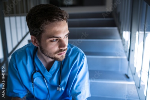 Thoughtful male nurse sitting on staircase