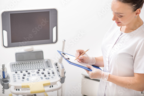 Cosmetologist making notes near ultrasound device