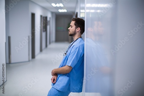 Tensed male nurse leaning on wall in corridor