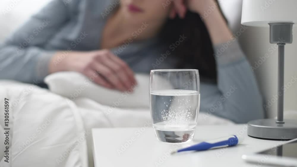 Sick woman lying in bed, she is putting an effervescent fizzing tablet into a glass of water, medicine and healthcare concept Sick woman lying in bed, she is putting an effervescent fizzing tablet into a glass of water, medicine and healthcare concept