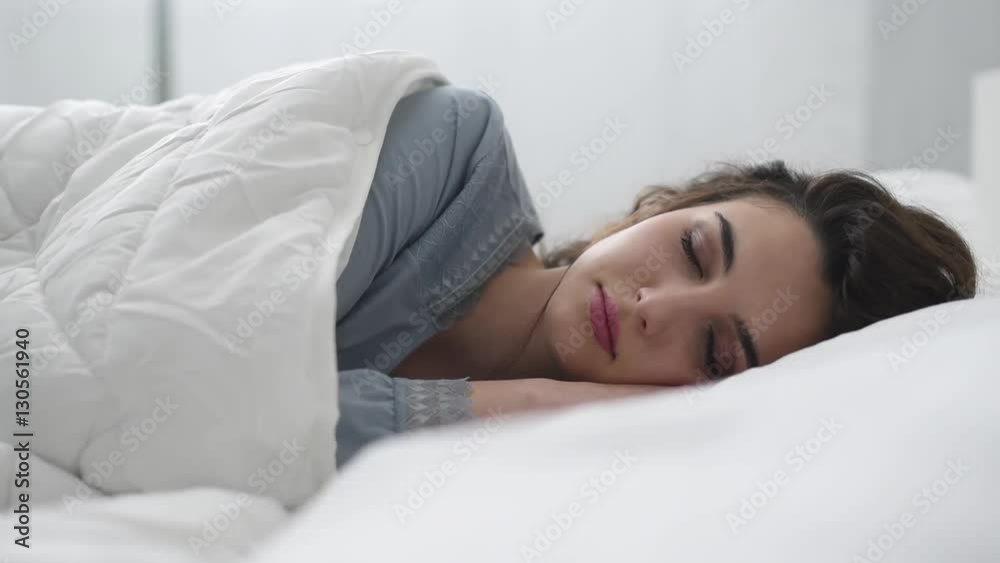 Young attractive woman waking up in her bed in the morning, she is smiling and opening her eyes Young attractive woman waking up in her bed in the morning, she is smiling and opening her eyes