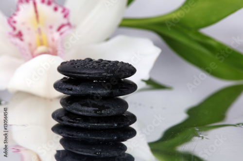 Spa background. Volcanic rock, bamboo and orchids on reflective background with raindrops. Relaxation, body care treatment, spa, wellness concept