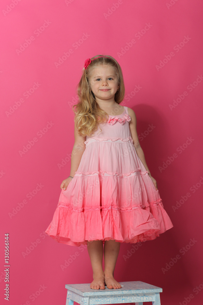 Little lady in dress standing on chair. Pink background Little lady in dress standing on chair. Pink background