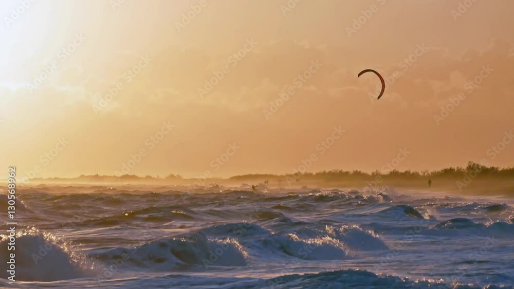 une voile de kitesurf sur une mer très agitée au coucher de soleil