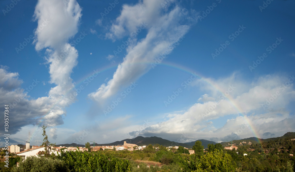 Real rainbow with cloudy sky over forest and field. Spain.