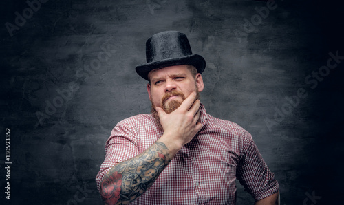 Bearded male with tattooed arms wearing top hat.