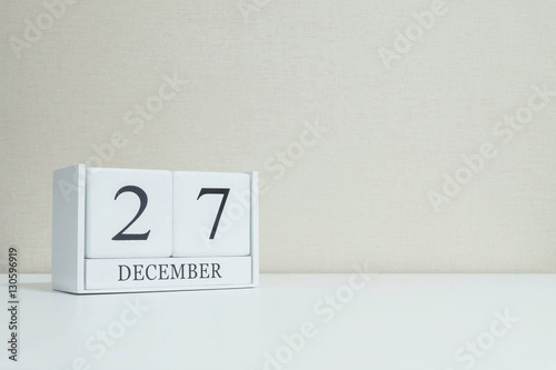 Closeup white wooden calendar with black 27 december word on blurred white wood desk and cream color wallpaper in room textured background with copy space , selective focus at the calendar