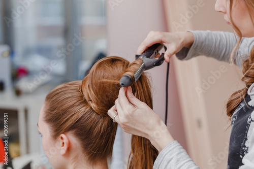 Pretty young woman is getting her brown hairs curls using the iron