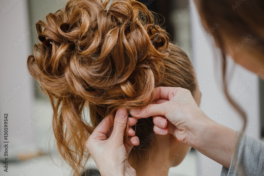 Naklejka premium Hairstylist makes the bride with blond hair beautiful high hairdress at the salon