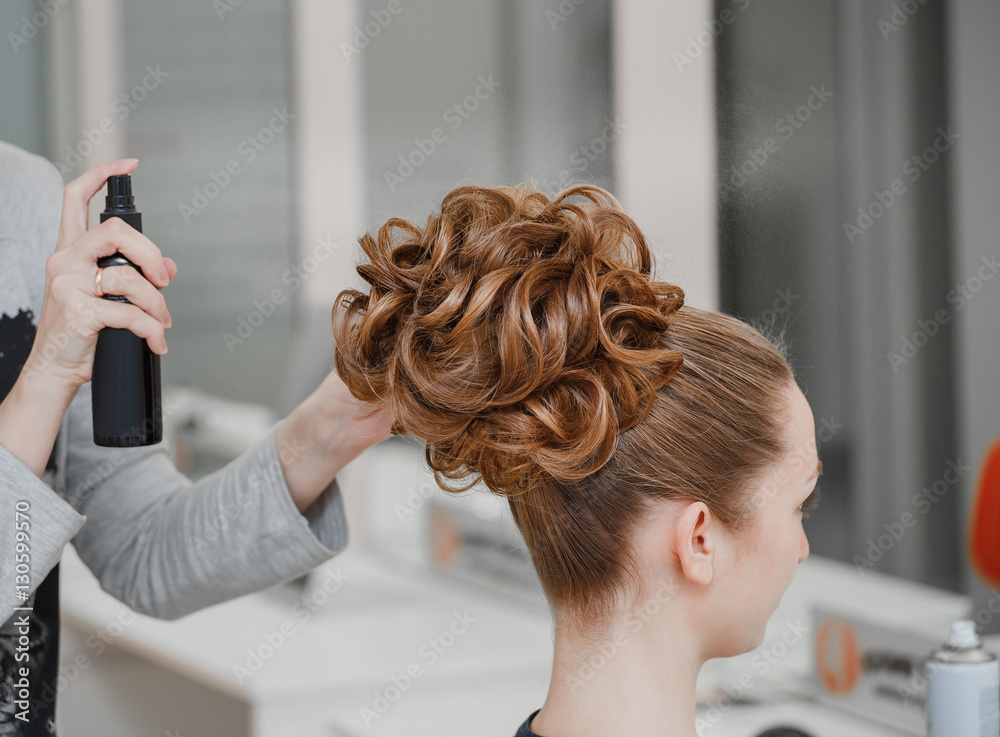 Fototapeta premium Closeup of hairdresser hands using hairspray styling on woman's healthy golden hair at barber salon