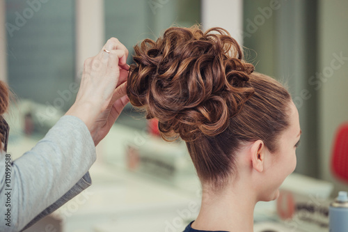 young woman making high bun hairstyle at hairdresser indoor shot