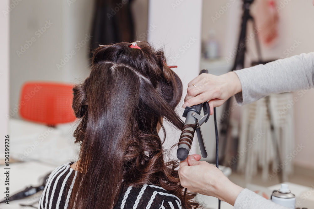 Fototapeta premium Hairdresser doing wrap curling brunette hair in a beauty salon with iron