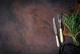 Vintage silverware with ivory handle, dark textile, wooden cutting board and bunch of fresh thyme on dark rusty background. Top view, copy space for text.