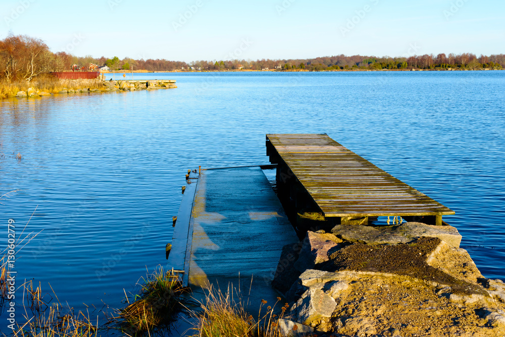 Wood and concrete combined to a dual pier. Surrounding water is windless and calm. Coastline visible in distance. Location Kuggeboda near Ronneby in Sweden.
