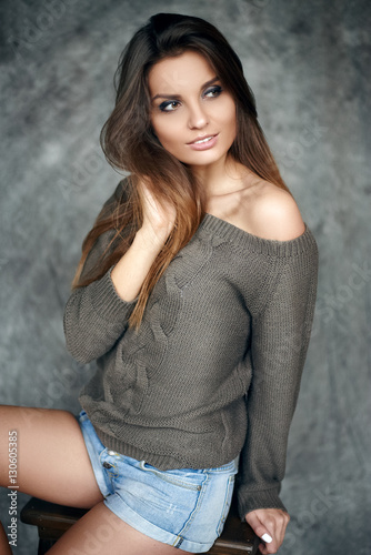 Portrait of a young and beautiful girl in sweater and denim shorts in the studio