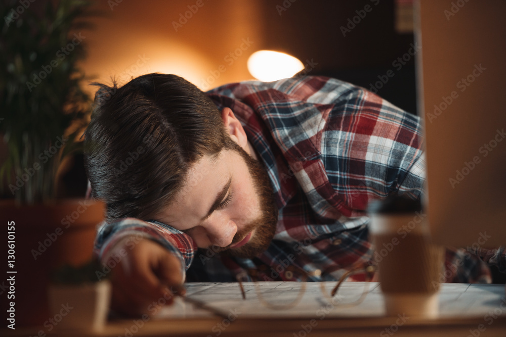 Tired bearded designer sleeping in office late at night