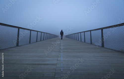 Tela Man walking on a modern footbridge into the morning fog of Lyon, France
