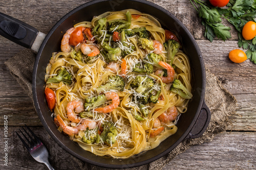 Pasta linguine with shrimps and broccoli in dripping pan on wooden background.
