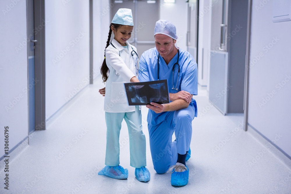 Smiling girl and doctor looking at x-ray in corridor