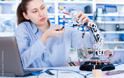 Girl in robotics laboratory. Young woman technician repair roboter manipulator