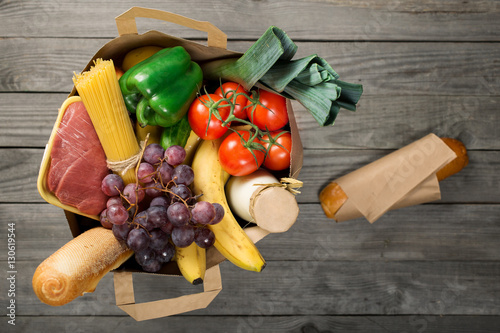 Full paper bag of food products on wooden background
