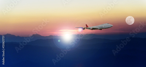 White passenger plane flying in the blue sky above the mountains