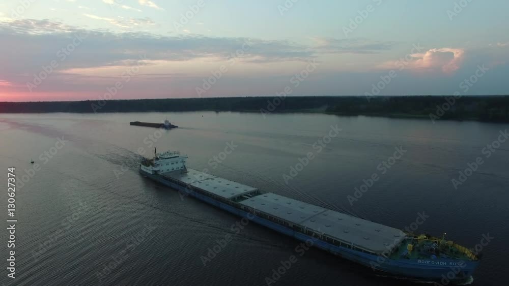 Cargo transport ship sailing on a wide river. Summer dawn. The camera movesh in the air away from the vessel. Another barge in background. Transportation on the river. Aerial view. Cargo transport ship sailing on a wide river. Summer dawn. The camera movesh in the air away from the vessel. Another barge in background. Transportation on the river. Aerial view.